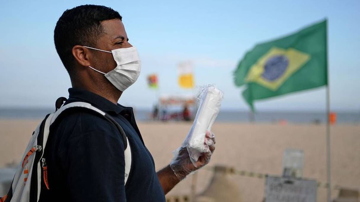 Au Brésil, un vendeur ambulant sur la plage de Copacabana, à Rio de Janeiro, porte un masque de protection contre le coronavirus. 
