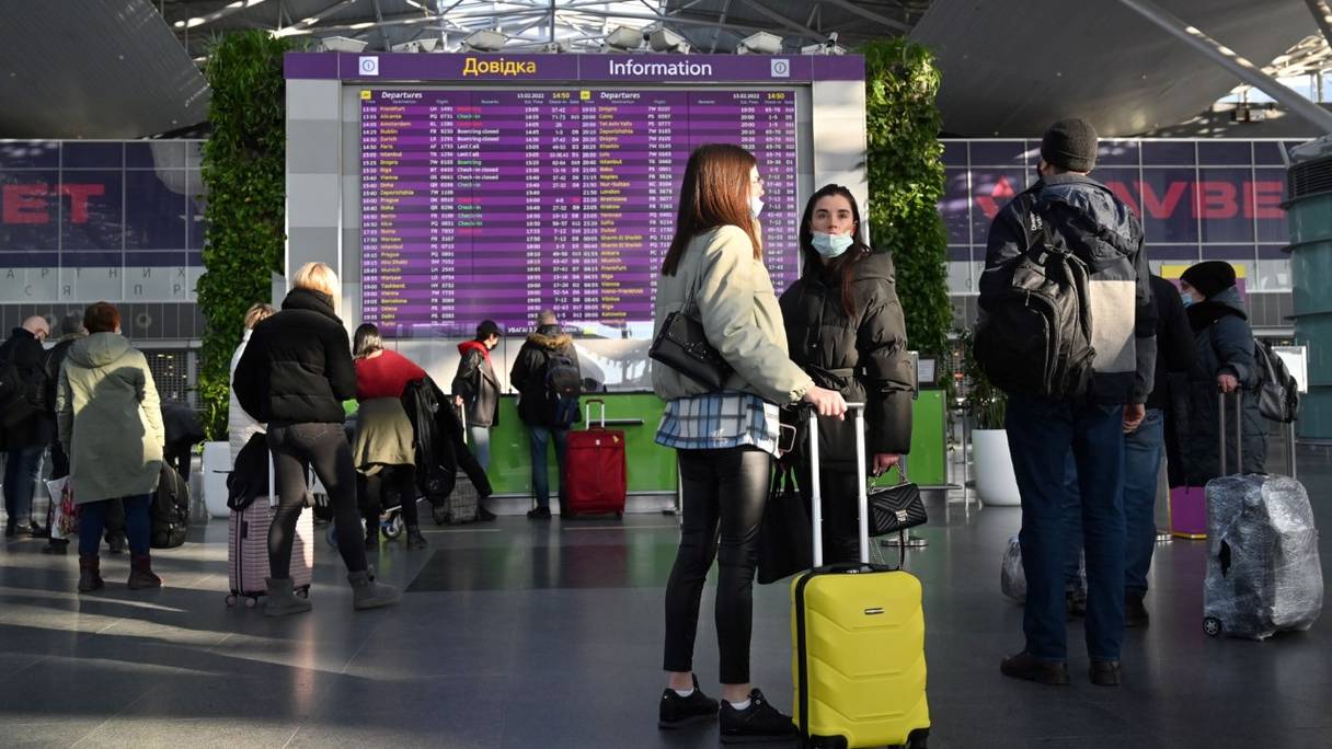 Des voyageurs attendent devant le tableau des départs leur vol à l'aéroport de Boryspil, à près de 30 kilomètres de Kiev, en Ukraine, le 13 février 2022.
