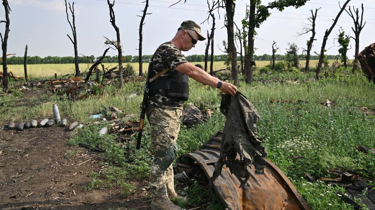 Un militaire ukrainien inspecte des débris à côté de véhicules militaires russes détruits sur un terrain non loin de la ville méridionale de Mykolaiev, le 12 juin 2022, au cours de l'invasion russe de l'Ukraine.
