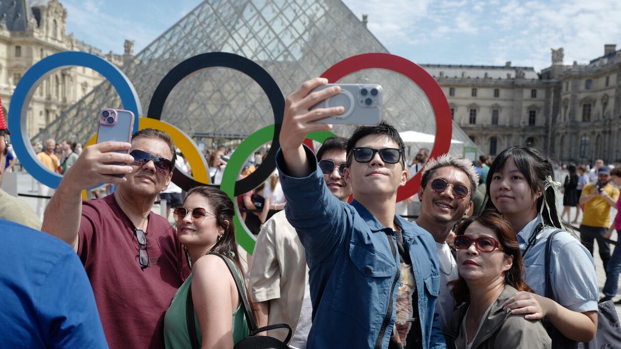 Des visiteurs devant la Pyramide du Louvre et les Anneaux Olympiques, dans le cadre des Jeux Olympiques de Paris 2024 à Paris, le 28 juillet 2024