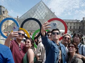 Des visiteurs devant la Pyramide du Louvre et les Anneaux Olympiques, dans le cadre des Jeux Olympiques de Paris 2024 à Paris, le 28 juillet 2024