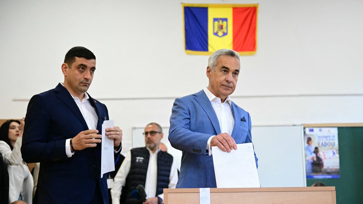 Le chef du parti nationaliste souverainiste « Alliance pour l'Union des Roumains » (AUR), George Simion (à gauche), attend que l'ancien candidat Calin Georgescu dépose son bulletin de vote lors du premier tour de l'élection présidentielle à Mogosoaia, le 4 mai 2025