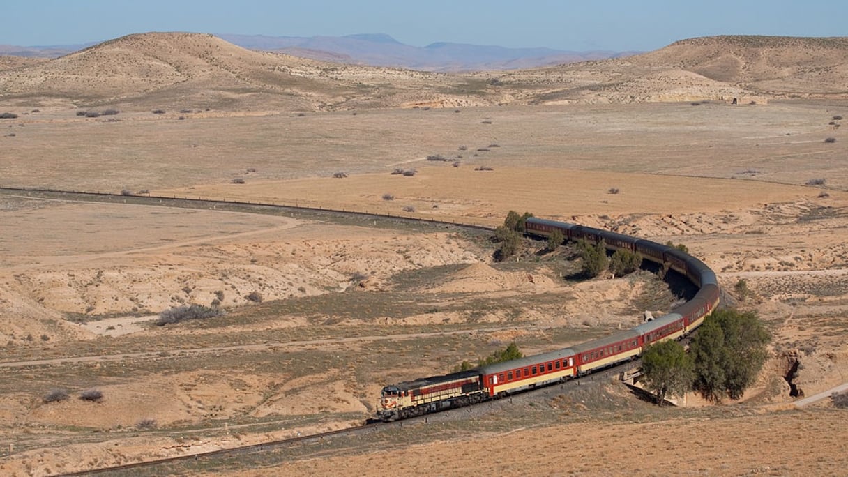 Près de oued Metlili, depuis la gare d'Oujda, une locomotive DH 370 (EMD GT26CW-2) de l'Office national des chemins de fer, avec un train transportant des voyageurs. L'ONCF fut créé le 1er janvier 1963 par le rachat de trois concessions qui exploitaient le réseau ferré marocain.