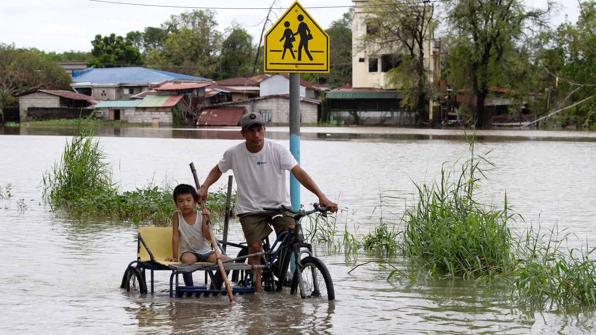 Un père et son enfant roulent en tricycle dans une rue inondée d'un village de la ville de Calumpit, dans la province de Bulacan, au nord de Manille, le 25 juillet 2025