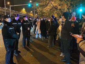 Des policiers surveillent des manifestants qui se rassemblent le long d'une rue, dans le contexte d'une série de manifestations contre les dures restrictions imposées par la Chine sur le Covid-19, à Pékin, le 28 novembre 2022.