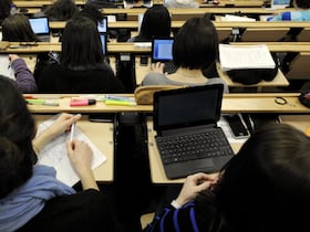 Des étudiants en cours magistral, à leur pupitre, dans un amphithéâtre d'université.