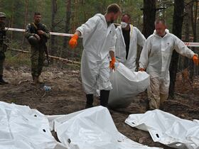 Des membres de la police scientifique ukrainienne portent une dépouille dans la forêt d'Izioum, dans l'est de l'Ukraine, le 16 septembre 2022.