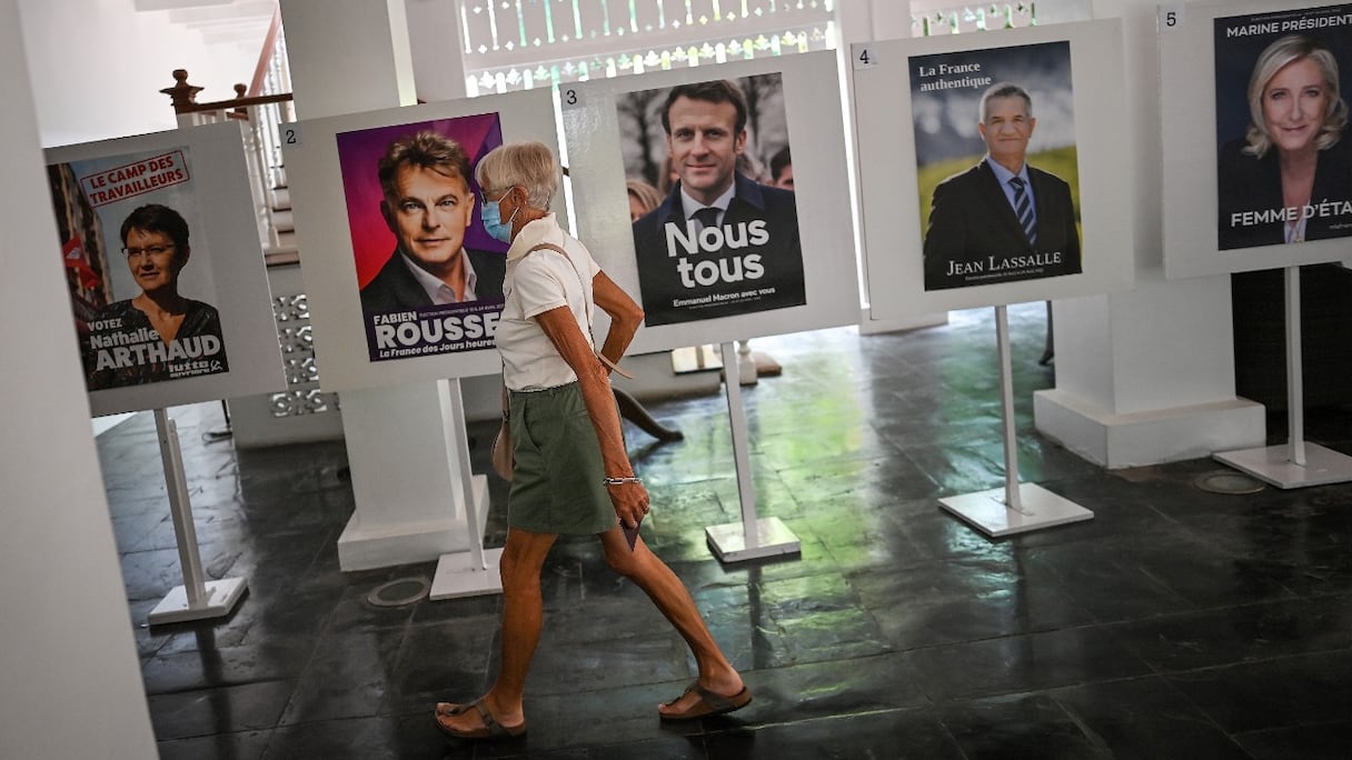 Une ressortissante française vivant en Thaïlande passe devant des affiches des candidats présidentiels français, avant de voter au premier tour des élections, à l'ambassade de France à Bangkok, le 10 avril 2022.
