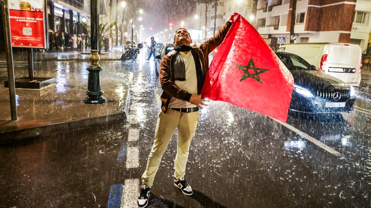 Un supporter marocain sous la pluie, tenant le drapeau national lors de la demi-finale de la Coupe du monde Qatar 2022 entre le Maroc et la France, à Rabat le 14 décembre 2022. 
