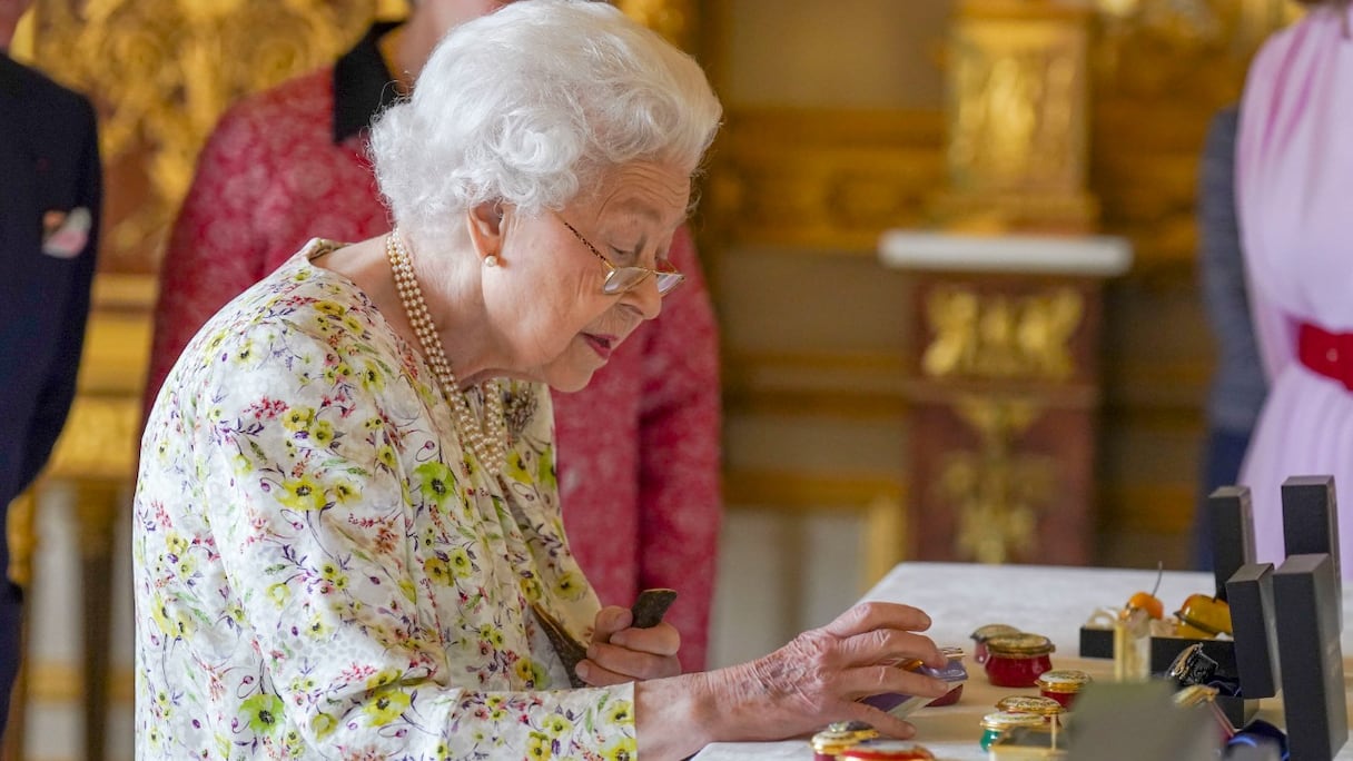 La reine Elizabeth II de Grande-Bretagne regarde une exposition d'artefacts de Halcyon Days pour commémorer le 70e anniversaire de l'entreprise dans le White Drawing Room du château de Windsor, le 23 mars 2022.
