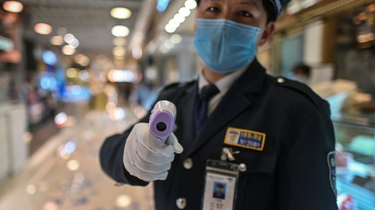 En Chine, un agent des forces de l'ordre, muni d'un détecteur de température, porte un masque de protection. 
