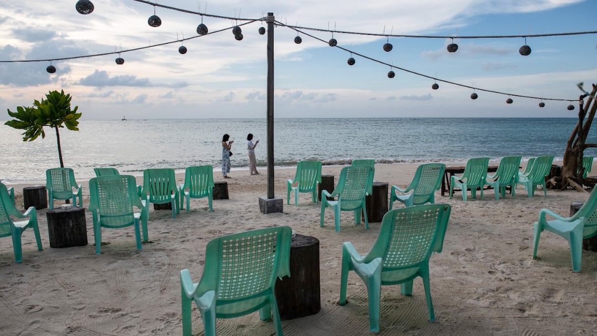 Des personnes marchent à côté de sièges vides disposés devant un bar sur une plage de Koh Phangan, dans le golfe de Thaïlande, le 26 novembre 2021.
