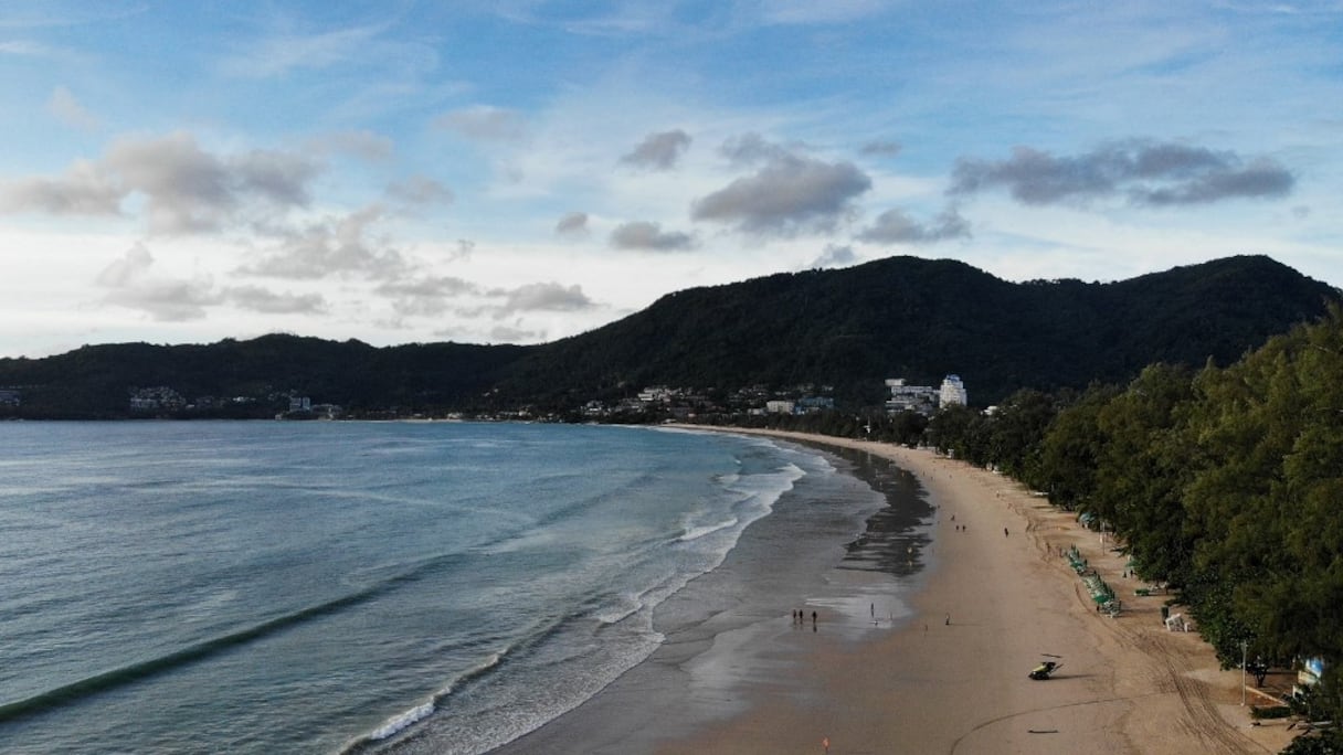 Quelques personnes marchent le long de la plage de Patong à Phuket, le 29 juin 2021 en Thaïlande, quelques jours avant le lancement du programme touristique «Phuket Sandbox», qui autorise les séjours de personnes vaccinées contre le coronavirus Covid-19, dès 1er juillet 2021. 
