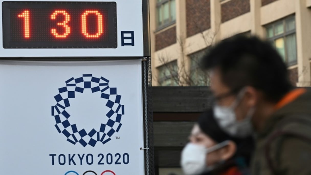 Des piétons portant un masque devant un panneau comptant les jours avant les Jeux olympiques de Tokyo, à Yokohama le 16 mars 2020.
