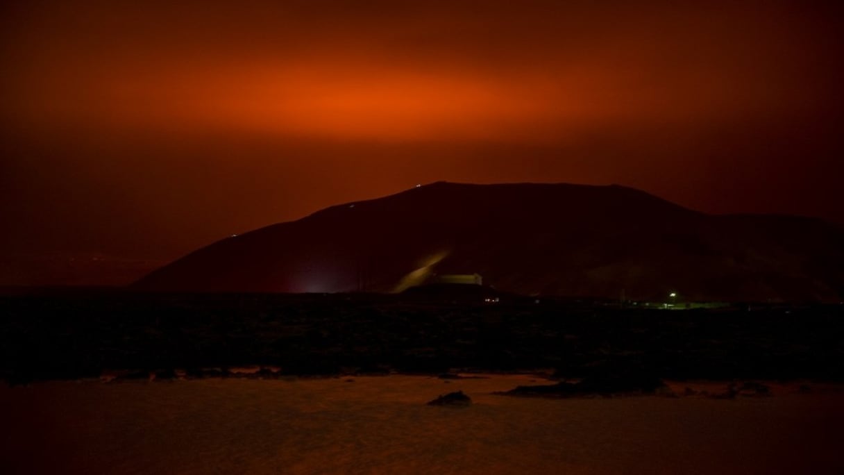 Miroitement rouge-orangé dans le ciel, provenant du magma s'écoulant du volcan en éruption Fagradalsfjall, derrière l'emblématique Blue Lagoon, à environ 45 km à l'ouest de la capitale islandaise, Reykjavik, le 19 mars 2021. 
