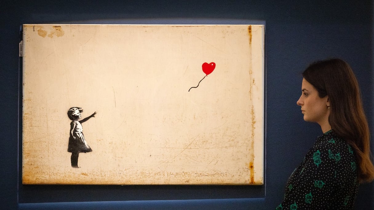 Un assistant de galerie pose à côté de «La Petite fille au ballon» de l'artiste britannique Banksy, lors d'un photocall avant une vente d'art moderne et contemporain, à la maison de vente aux enchères Sotheby's, à Londres, le 22 février 2022.
