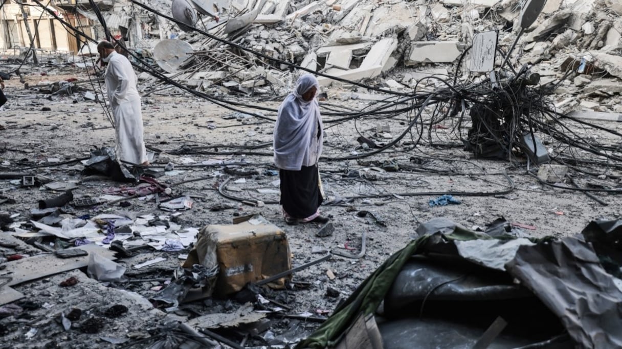 Des Palestiniens marchent au milieu des débris près de la tour al-Sharouk, qui abritait le bureau de la chaîne de TV Al-Aqsa dans la bande de Gaza contrôlée par le Hamas, après avoir été détruite par une frappe aérienne israélienne, le 13 mai 2021. 
