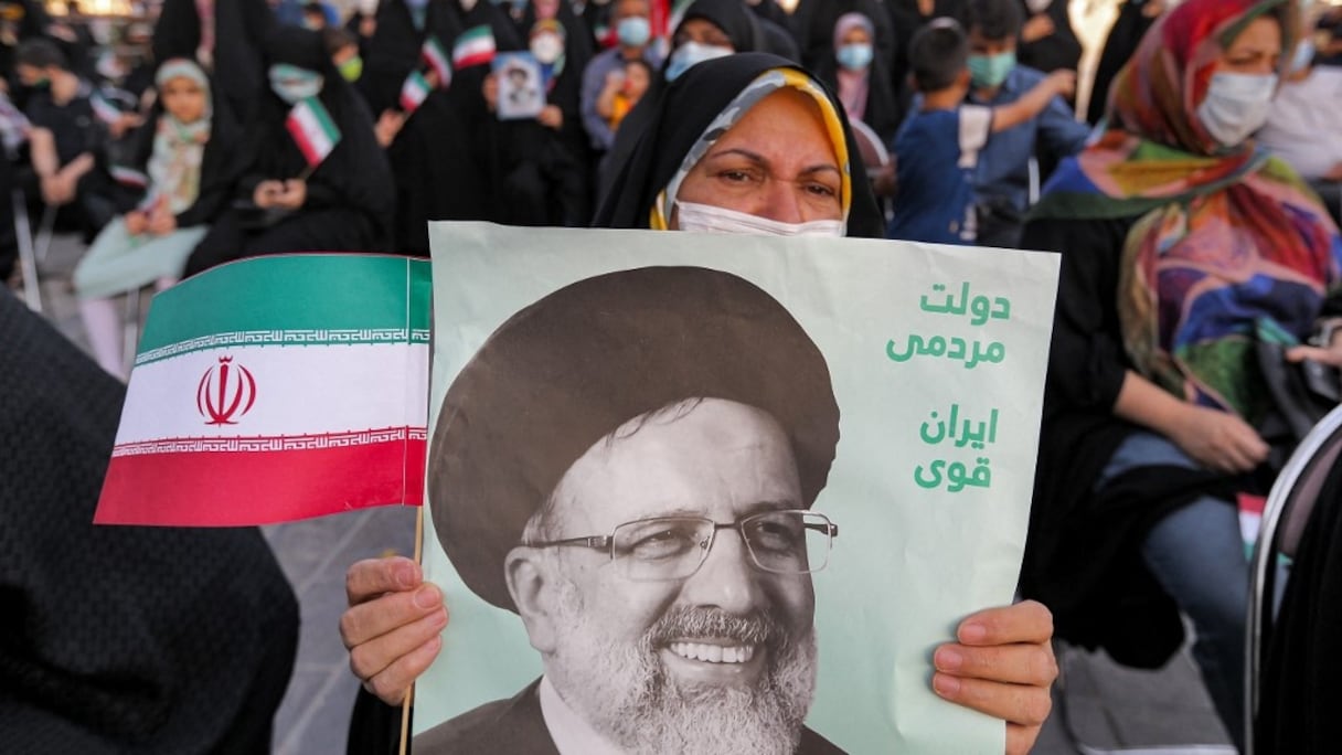 Une femme tient une affiche du président iranien nouvellement élu Ebrahim Raïssi, avec un texte en persan "gouvernement du peuple, Iran fort", alors que ses partisans célèbrent sa victoire sur la place Imam Hussein dans la capitale Téhéran, le 19 juin 2021.
