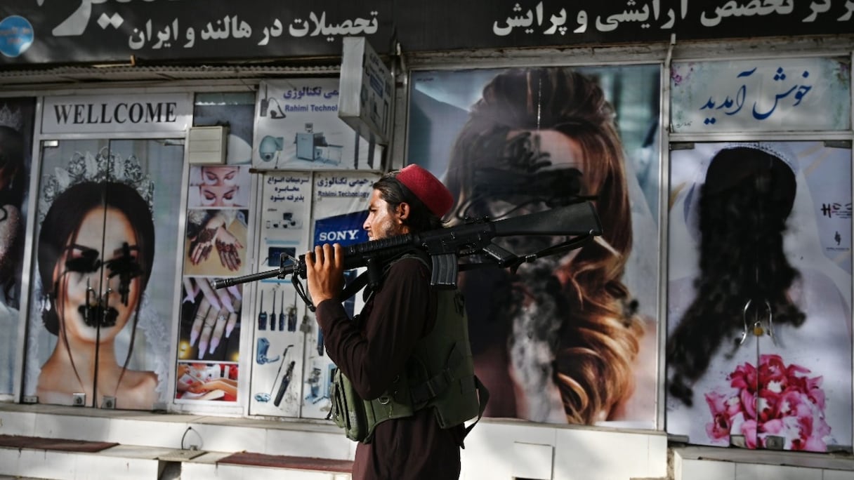 Un combattant taliban passe devant un salon de beauté où les affiches représentant des visages de femmes ont été défigurés avec de la peinture en aérosol, à Shar-e-Naw, à Kaboul, le 18 août 2021.
