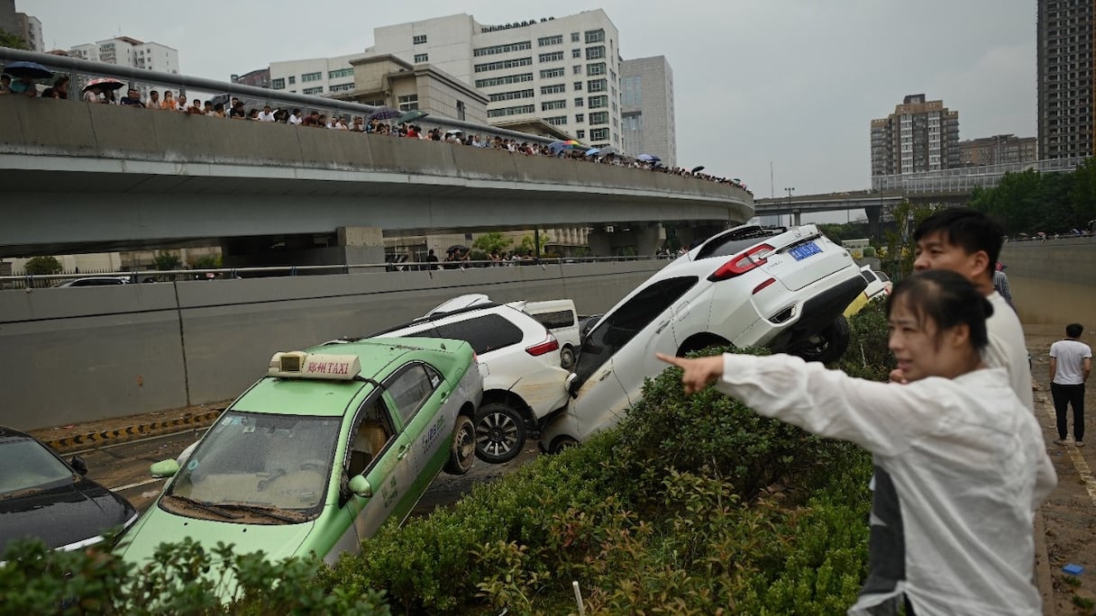 Des personnes regardent des voitures immobilisées dans les eaux de crue à la suite de fortes pluies, à Zhengzhou, dans la province centrale du Henan, en Chine, le 22 juillet 2021.
