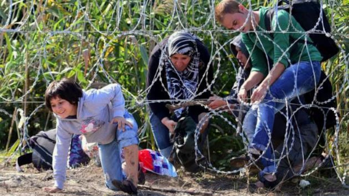 Une famille de migrants franchit une clôture de barbelés le 28 août 2015, à Roszke à la frontière entre la Hongrie et le Serbie.
