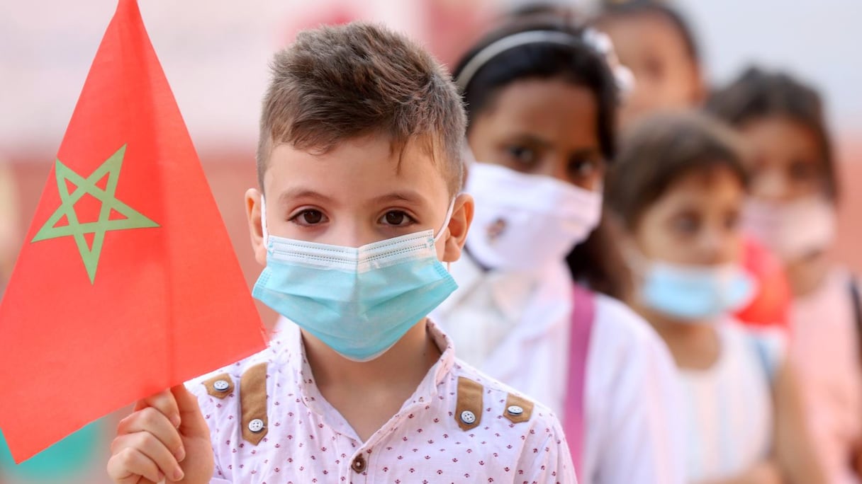 Un élève tient le drapeau marocain alors que retentit l’hymne national, le 1er octobre 2021 à Marrakech, marquant ainsi une rentrée scolaire pleine d'enthousiasme. 
