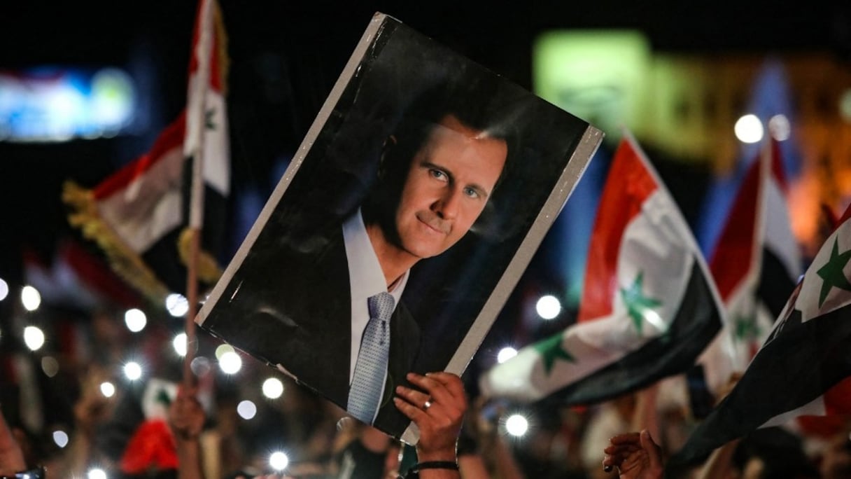 Des Syriens agitent des drapeaux et brandissent un portrait de leur président alors qu'ils célèbrent dans les rues de la capitale, Damas, un jour après l'élection présidentielle, le quatrième mandat de l'actuel président Bachar al-Assad, le 27 mai 2021. 
