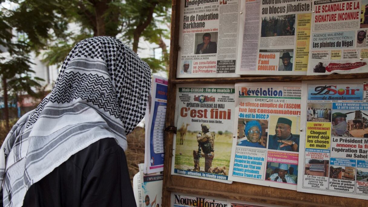 Un homme coiffé d'un keffieh regarde le le 11 juin 2021 à Bamako regarde les titres de l'actualité annonçant le retrait de la présence militaire française au Sahel, où ces forces ont combattu les djihadistes depuis près d'une décennie.
