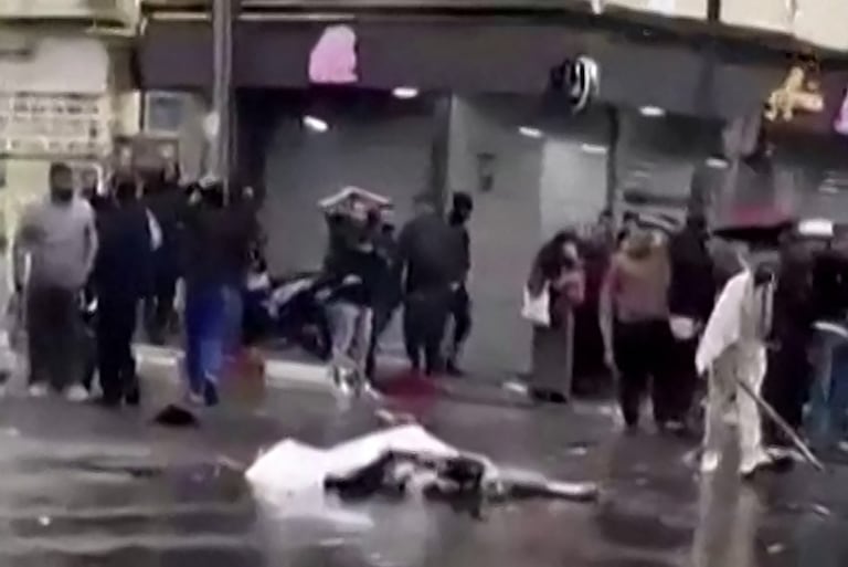 Une capture vidéo à partir d'images publiées sur les réseaux sociaux le 13 avril 2026, montrant des passants debout près d'un corps recouvert gisant au milieu d'une rue à Blida.