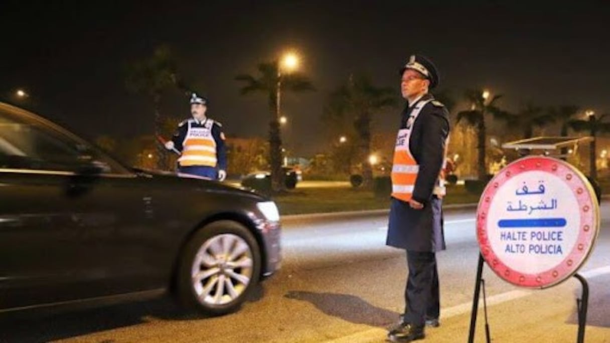 Un point de barrage policier, de nuit. 
