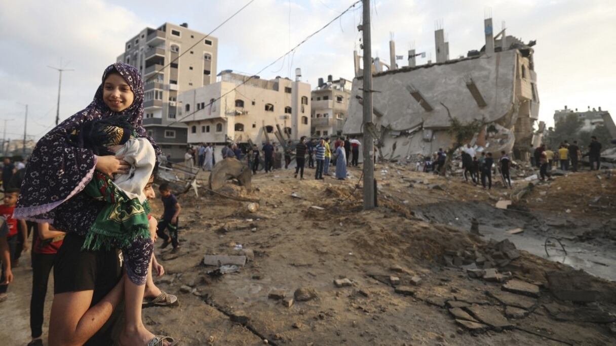 Une Palestinienne porte un bébé dans ses bras alors que des gens se rassemblent à l'extérieur pour échanger leurs souhaits de vacances de l'Aïd al-Fitr au milieu de la destruction de la ville de Beit Lahia, au nord de la bande de Gaza, le 13 mai 2021.
