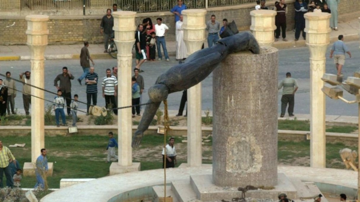 Les Irakiens regardent le déboulonnement à Bagdad de la statue du président Saddam Hussein, après son renversement consécutif à l'invasion américaine de l'Irak, le 9 avril 2003.
