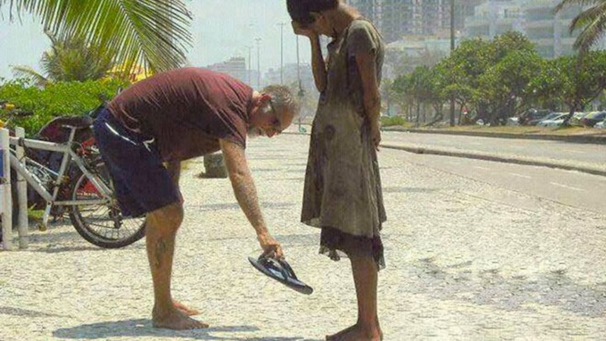Un homme offre ses chaussures à une jeune sans-abri aux pieds nus.
