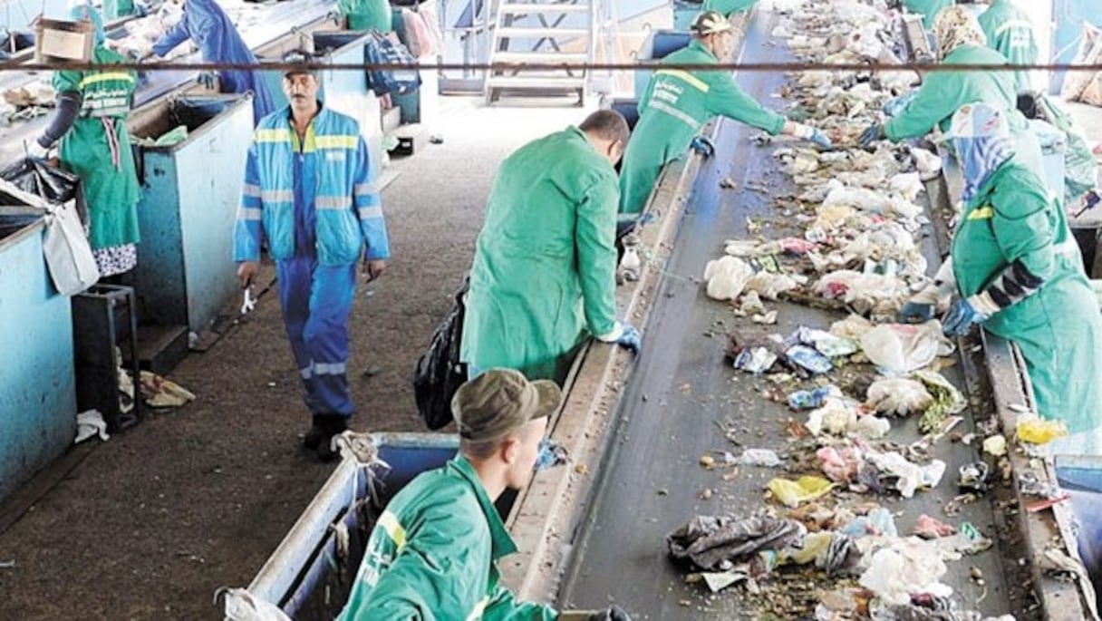 Plusieurs agents triant des déchets ménagers sur un tapis convoyeur.
