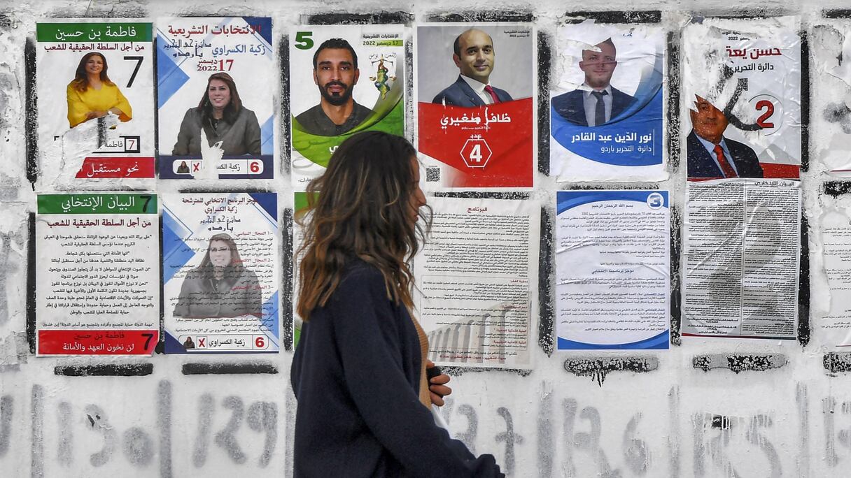 Un jeune femme passe devant des affiches de candidats à l'élection nationale tunisienne prévue ce 17 décembre, collées sur un mur le long d'une route à Tunis.
