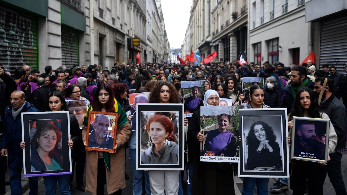 Des manifestants tiennent les portraits des victimes de la fusillade de la rue d'Enghien à Paris le 23 décembre 2022, et de celles des meurtres de la rue La Fayette en 2013, lors d'une marche pour leur rendre hommage et en solidarité avec la communauté kurde de Paris, le 26 décembre 2022. 
