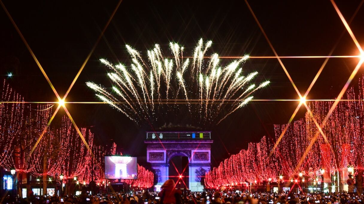 Des personnes prennent des photos du feu d'artifice qui éclate dans le ciel, le 31 décembre 2019 au-dessus de l'Arc de Triomphe lors des festivités du nouvel an sur l'avenue des Champs-Élysées, à Paris.
