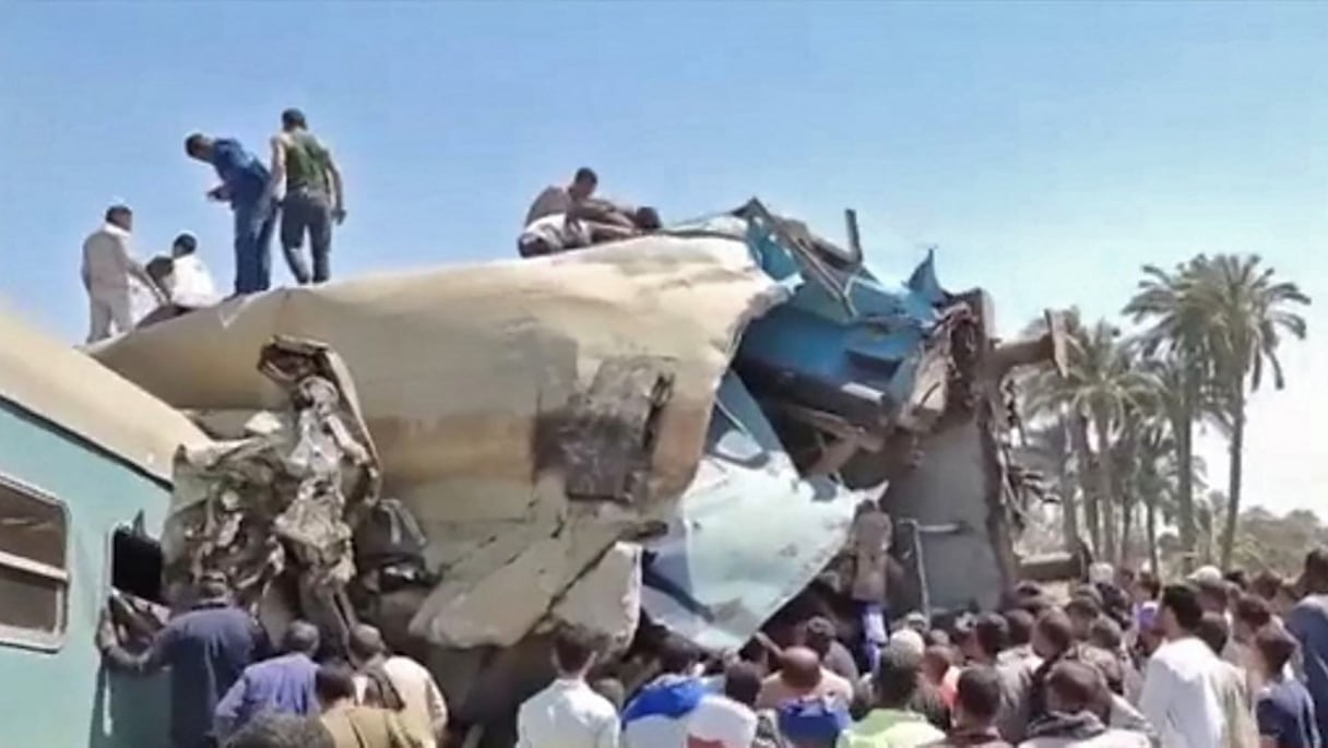 Cette capture vidéo prise de la chaîne de télévision d'Etat égyptienne montre des personnes rassemblées autour des épaves de deux trains entrés en collision dans le district de Tahta de la province de Sohag, à quelque 460 km au sud du Caire, le 26 mars 2021.
