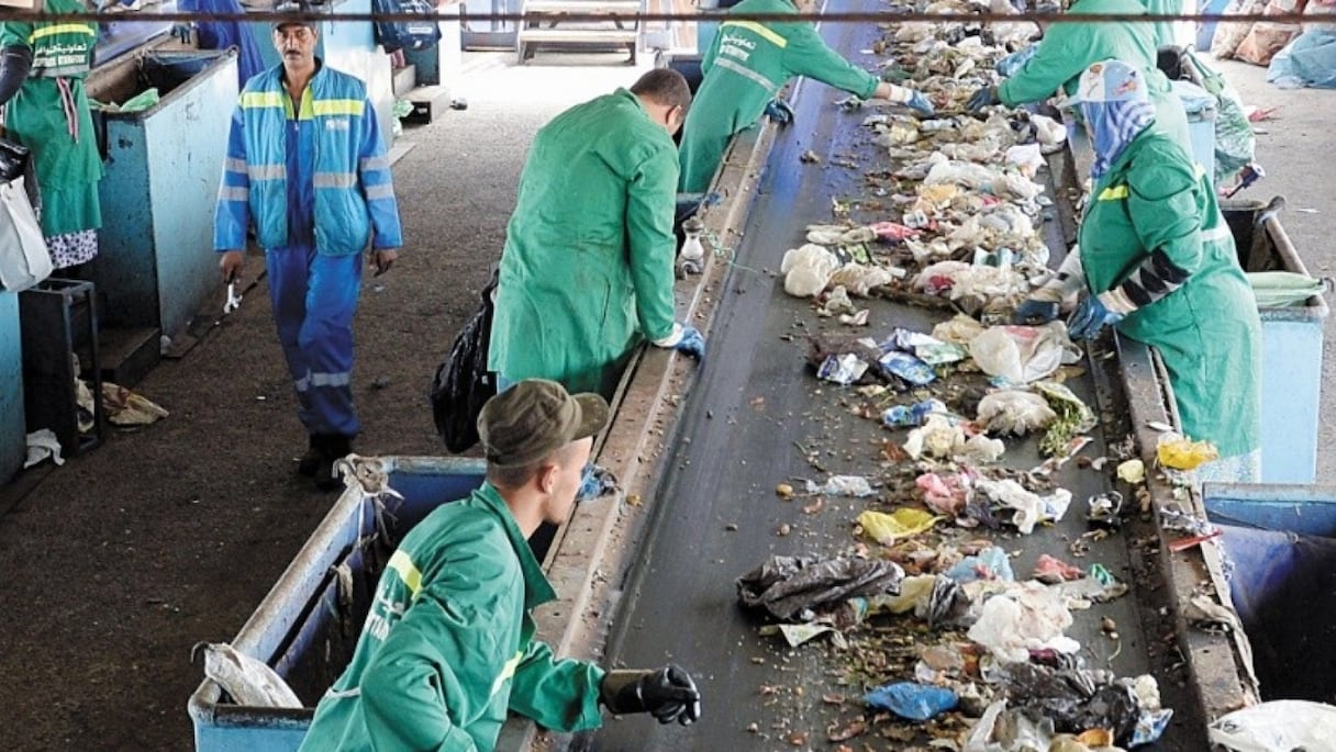 Plusieurs agents triant des déchets ménagers sur un tapis convoyeur.
