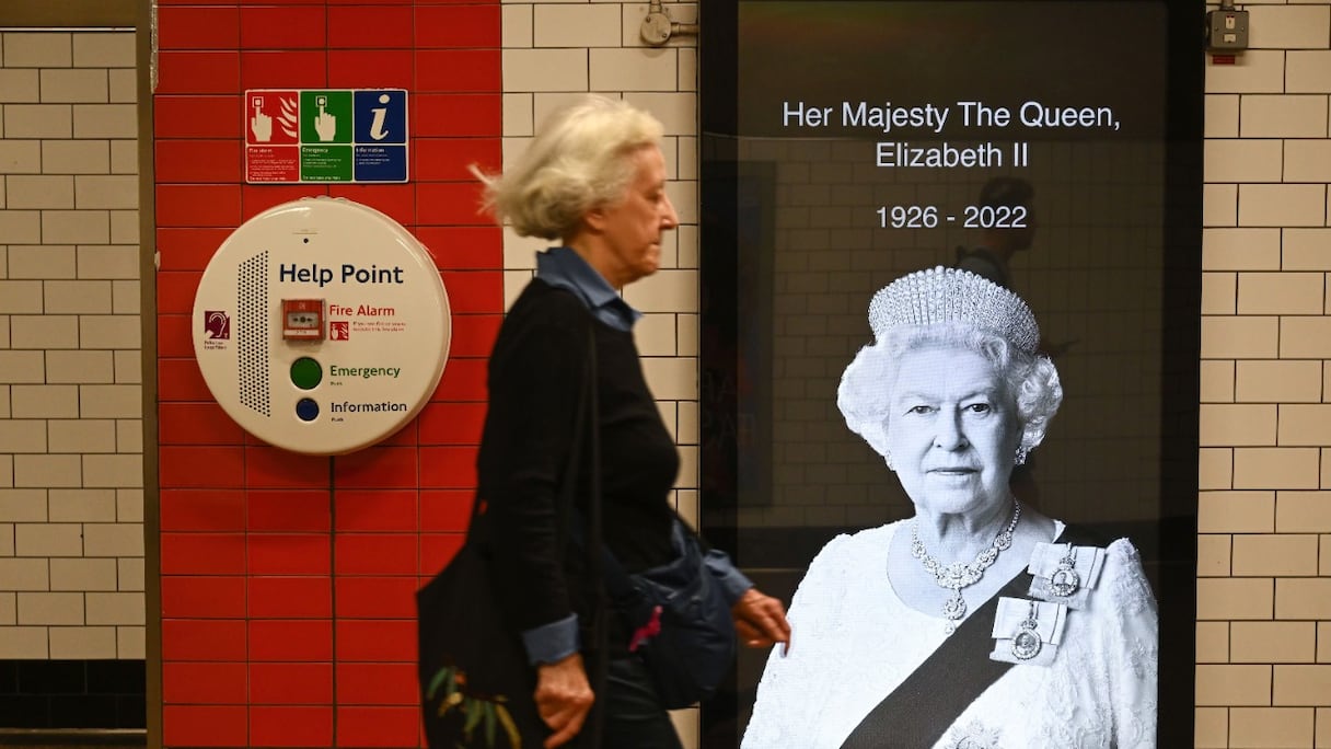 Une femme passe devant une photo de la reine Elizabeth II de Grande-Bretagne dans le métro de Londres, le 10 septembre 2022, deux jours après sa mort à l'âge de 96 ans.
