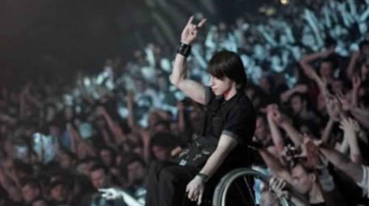 Le public aide un jeune homme en fauteuil roulant à profiter d'un concert.
