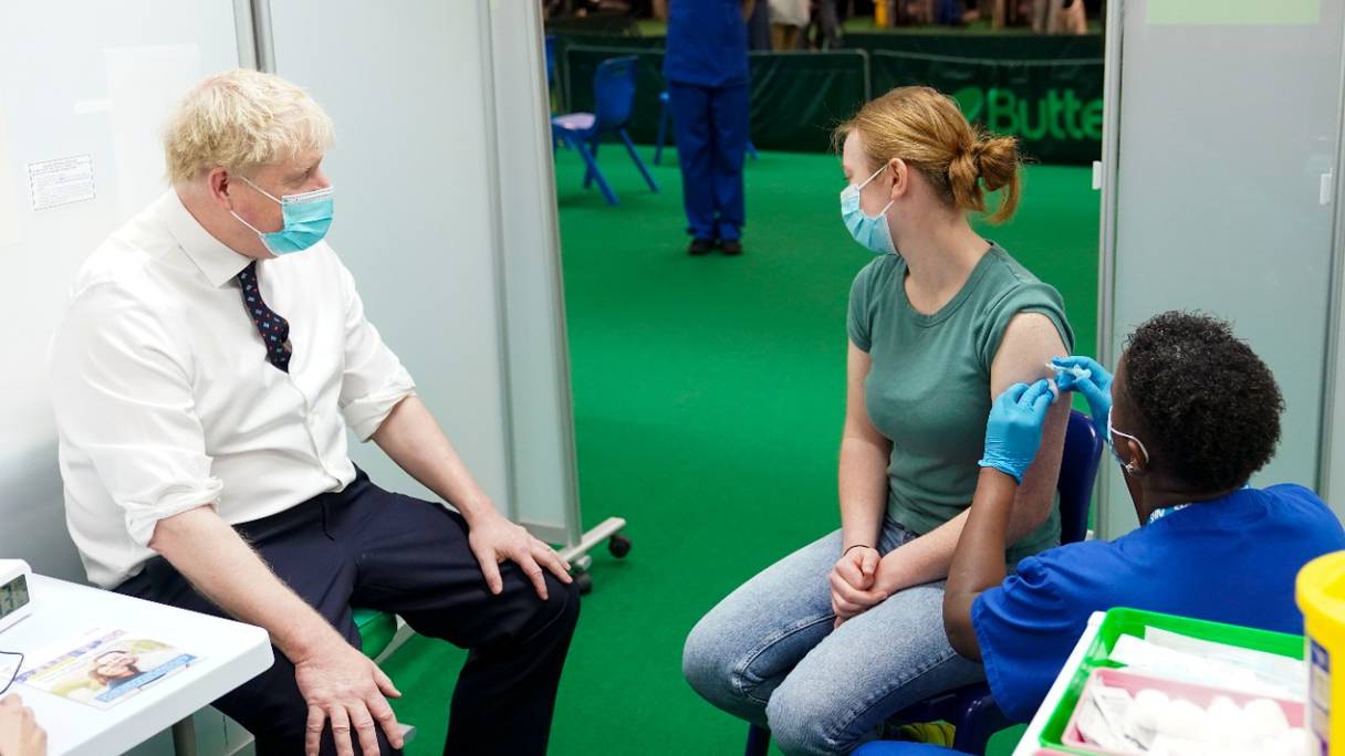 Le Premier ministre britannique Boris Johnson, portant un masque sanitaire, regarde une personne se faire vacciner contre le Covid-19 à Aylesbury, au nord-ouest de Londres, le 3 janvier 2022.
