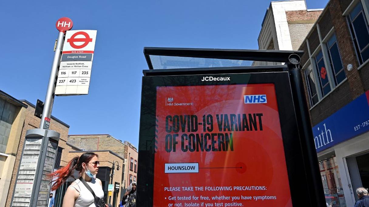 Une femme attend à un arrêt de bus près d'un panneau avertissant les membres du public d'une "variante de coronavirus préoccupante" à Hounslow, dans l'ouest de Londres, le 1er juin 2021. 
