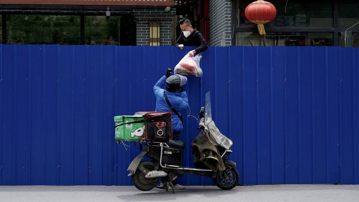 Un livreur passe des articles à un homme à l'intérieur d'une zone résidentielle clôturée, dans un quartier confiné de Pékin, le 11 mai 2022.
